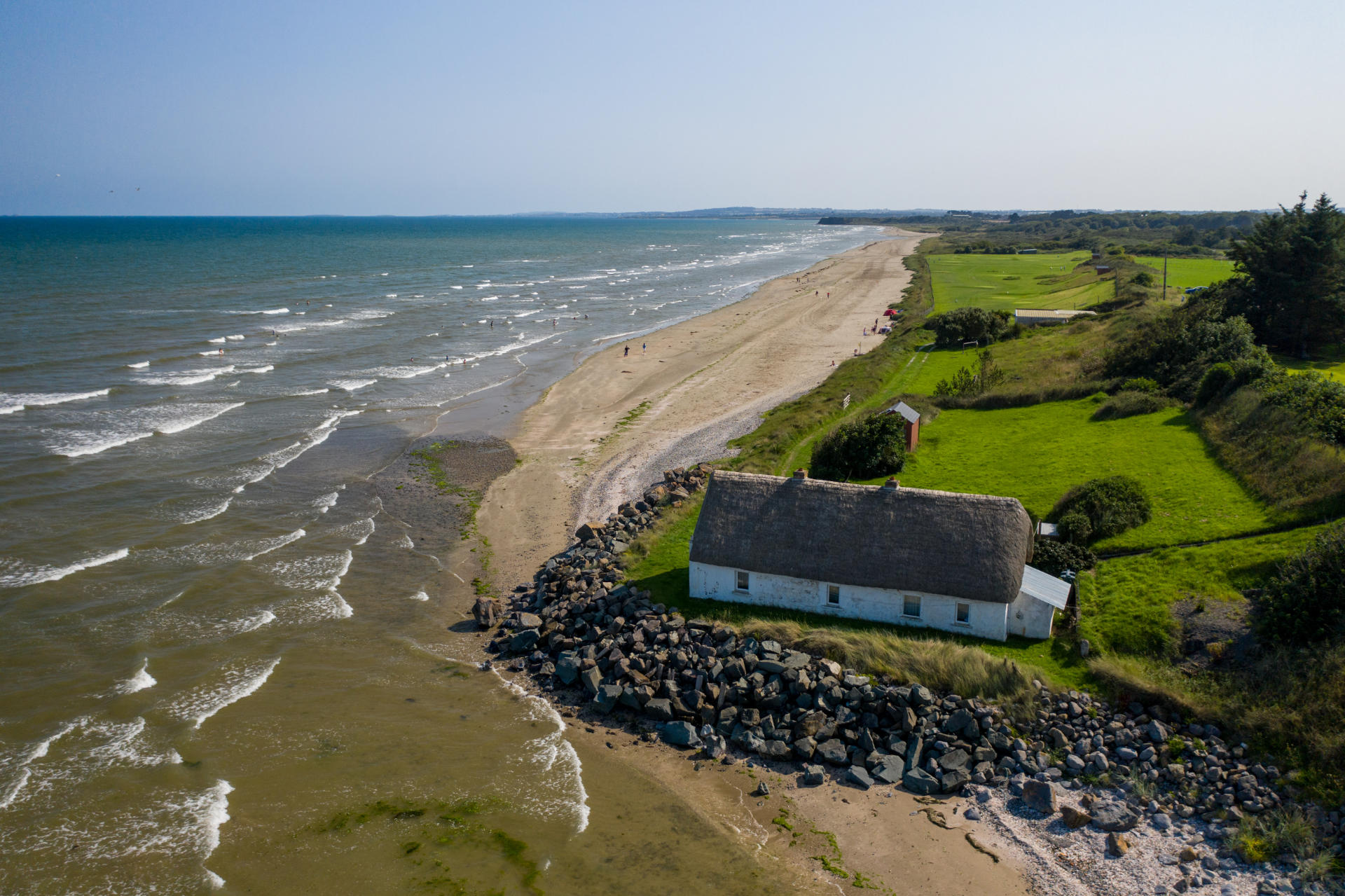 Aerial view of ocean waves hitting the coast near a lone cottage.